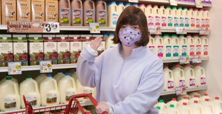 Young woman wearing mask waving in grocery store (Trader Joe's).